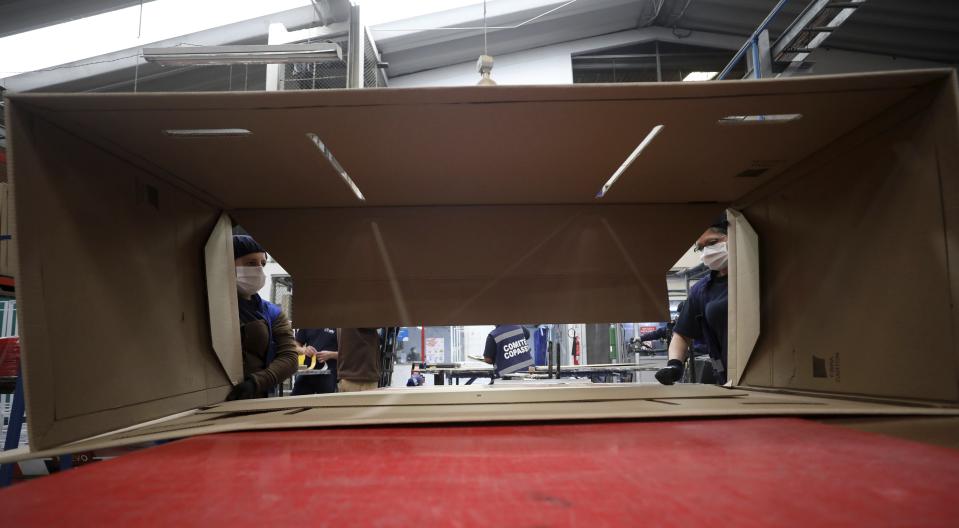 Workers at a company that designs packaging for product displays assemble a cardboard box designed to serve as both a hospital bed and a coffin, intended for COVID-19 patients, in Bogota, Colombia, Friday, May 8, 2020. Owner Rodolfo Gomez said he plans to donate the first units to Colombia's Amazonas state, and that the company will sell others to small hospitals for 87 dollars. (AP Photo/Fernando Vergara)