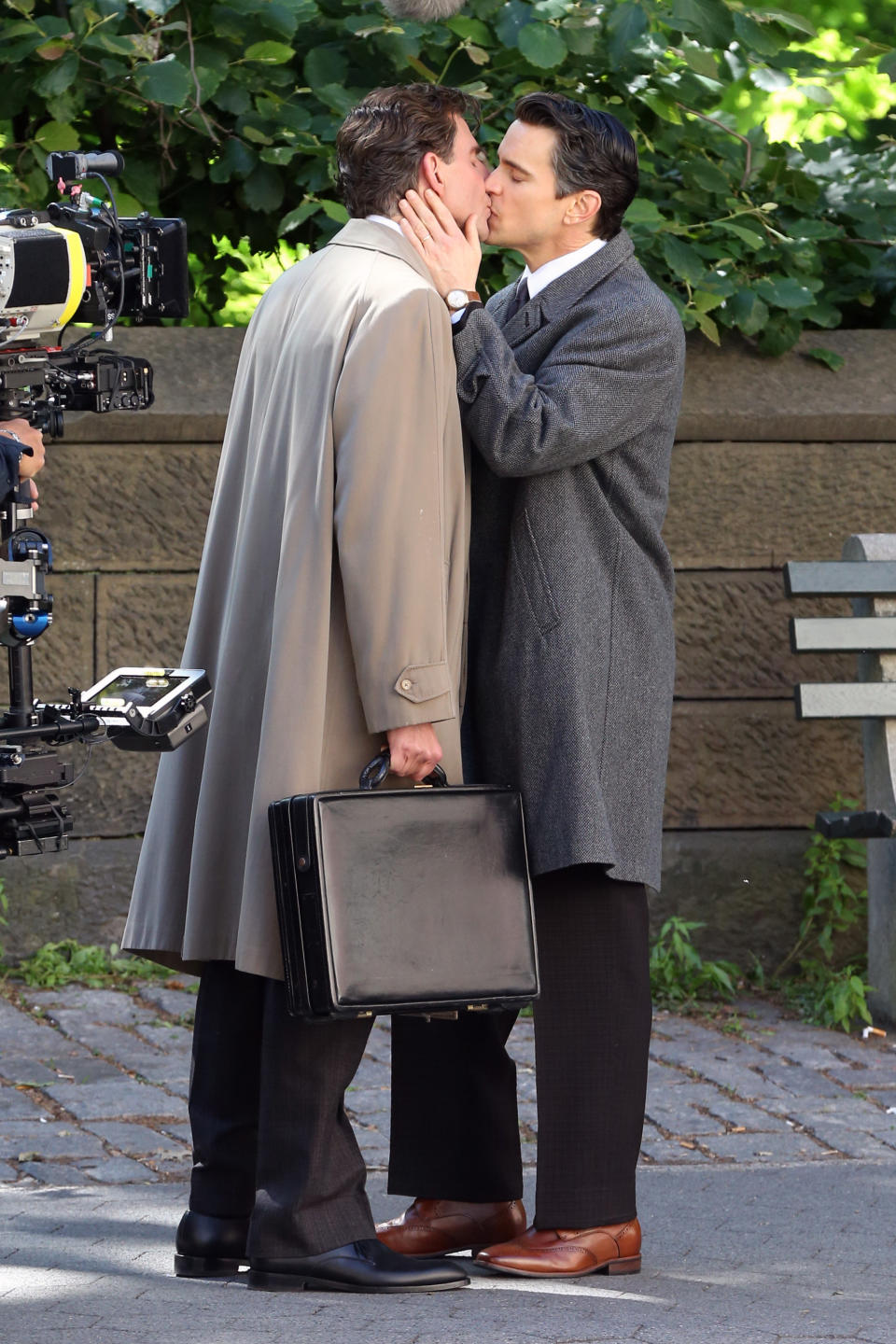 Matt holds Bradley's face as they kiss while standing on a sidewalk and Bradley holds a briefcase