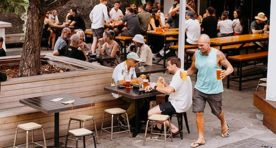 A man carrying two beers back to a table in a beer garden.