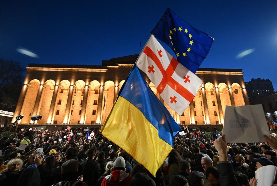 Against the illuminated colonnades of the Parliament, protesters gather.