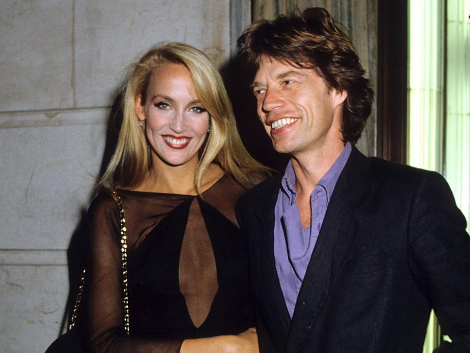 Jerry smiling in a sheer black dress and Mick smiling in a blazer and purple shirt.