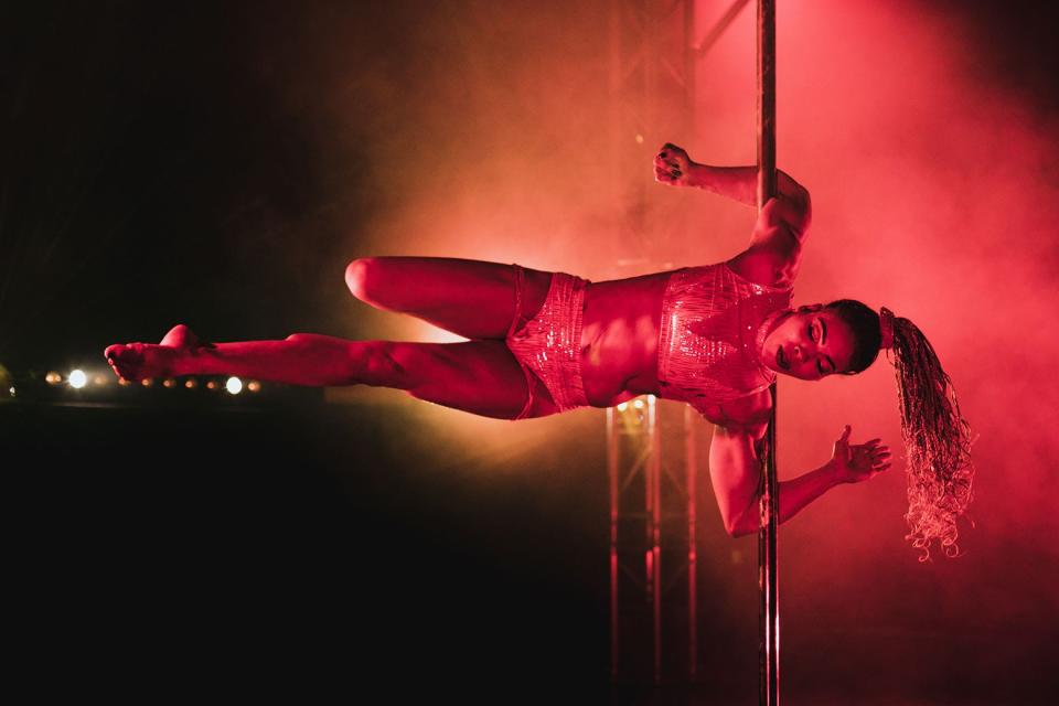 A woman balancing herself with her arms horizontally on a pole.