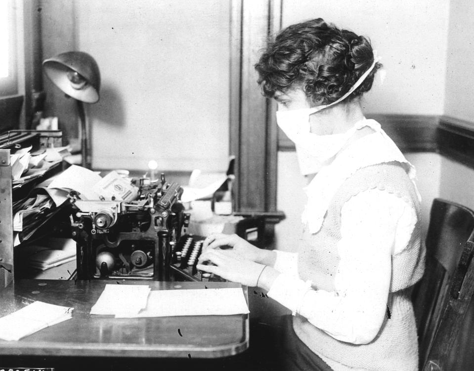 A typist wears mask while working at her office desk, during the influenza epidemic, 1918. (Photo by PhotoQuest/Getty Images)