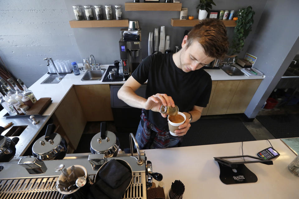 FILE - In this Nov. 4, 2019, file photo barista Porter Hahn makes an iced coffee drink for a customer in a coffee shop in Seattle. As of Jan. 1, 2020, there are higher minimum wages in a quarter of the states, and new federal overtime rules. (AP Photo/Elaine Thompson, File)