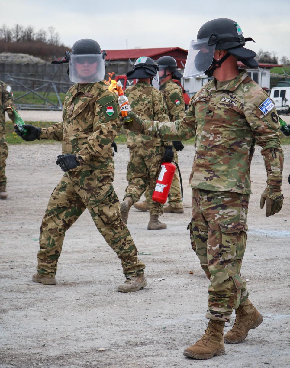 A photo of two soldiers wearing face shields, helmets, and army fatigues, holding Molotov cocktails in their right hands.