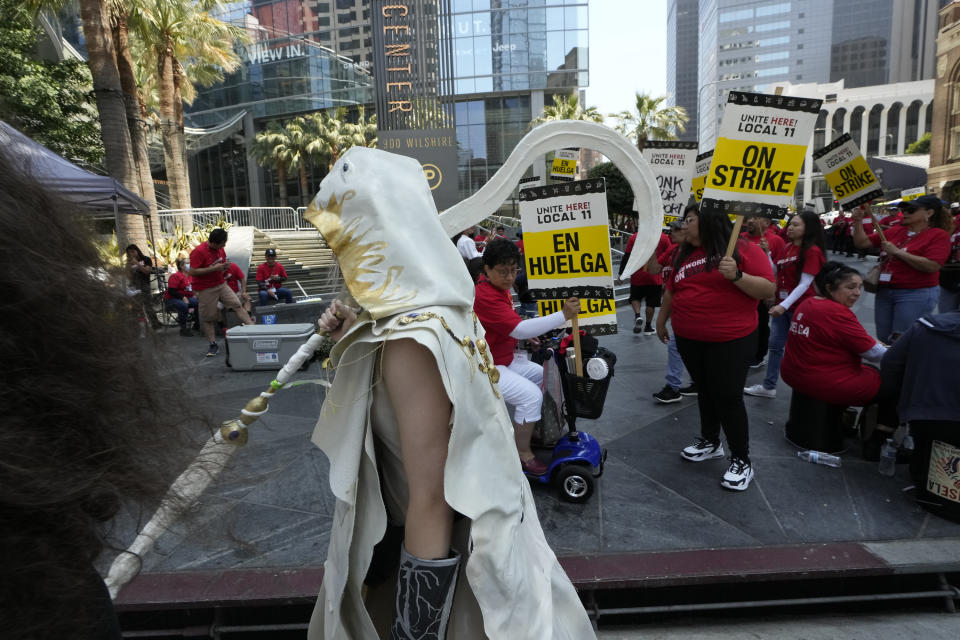A tourist, in a costume, walks past striking hotel workers rallying outside the Intercontinental Hotel on Monday, July 3, 2023, in downtown Los Angeles. (AP Photo/Damian Dovarganes)