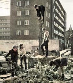 A colourised black and white shot of children outside with stuff in front of a tall building.