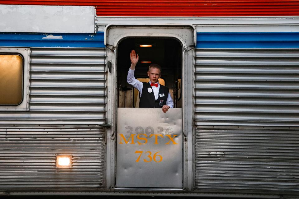 Volunteer car host Alex Kuffer, of Lansing, 14, waves as the North Pole Express train cars travel by Wrought Iron Grill in Owosso on Saturday, Nov. 18, 2023.