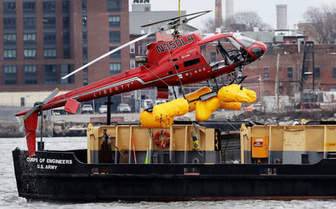 The helicopter is hoisted by crane from the East River onto a barge, Monday, March 12 - Credit: Mark Lennihan/AP