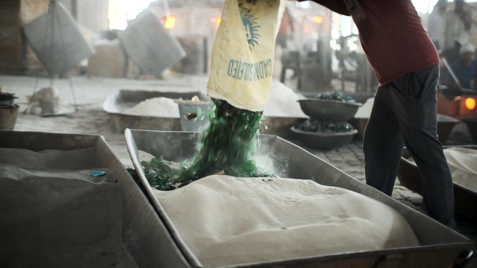 A worker dumps broken glass into a tray of sand