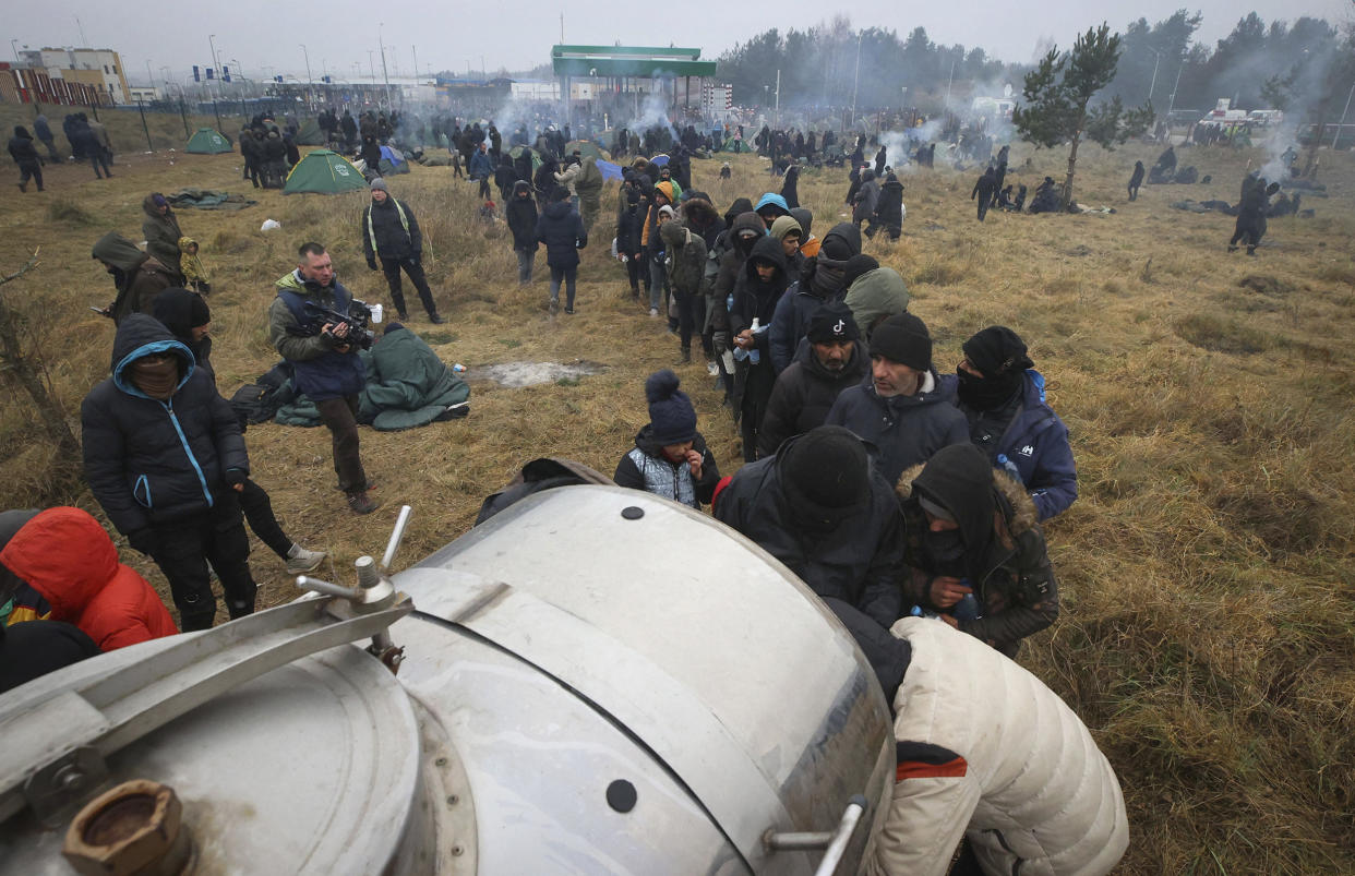 Migrants from the Middle East and elsewhere stand in line to a drinking water tank at the Belarus-Poland border near Grodno, Belarus, on Tuesday, Nov. 16, 2021. The EU is calling for humanitarian aid as up to 4,000 migrants are stuck in makeshift camps in freezing weather in Belarus while Poland has reinforced its border with 15,000 soldiers, in addition to border guards and police. (Leonid Shcheglov/BelTA via AP)
