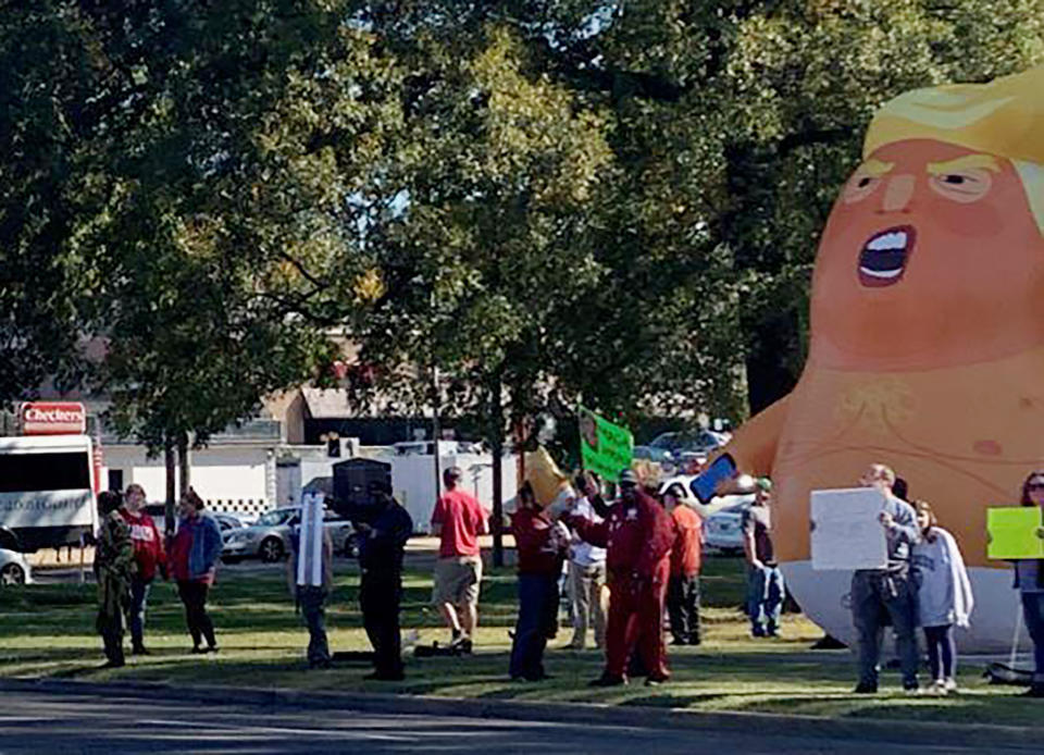 People standing by a Baby Trump balloon at Monnish Park protest President Donald Trump's visit to an NCAA college football game between Louisiana State and Alabama playing nearby in Tuscaloosa, Ala., Saturday, Nov. 9, 2019. The towering Baby Trump protest balloon was knifed and deflated by someone unhappy with its appearance during Trump's trip to Alabama, organizers said. (Stephanie Taylor/The Tuscaloosa News via AP)