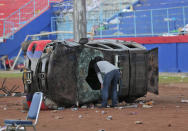 A plain-clothed police officer inspects a police car wrecked in soccer riots at Kanjuruhan Stadium in Malang, East Java, Indonesia, Sunday, Oct. 2, 2022. Panic at an Indonesian soccer match Saturday left over 150 people dead, most of whom were trampled to death after police fired tear gas to dispel the riots. (AP Photo/Trisnadi)