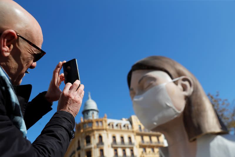 A man takes pictures of a monument displayed with a protective mask, after regional authorities postponed the Fallas Festival amidst coronavirus concerns in Valencia