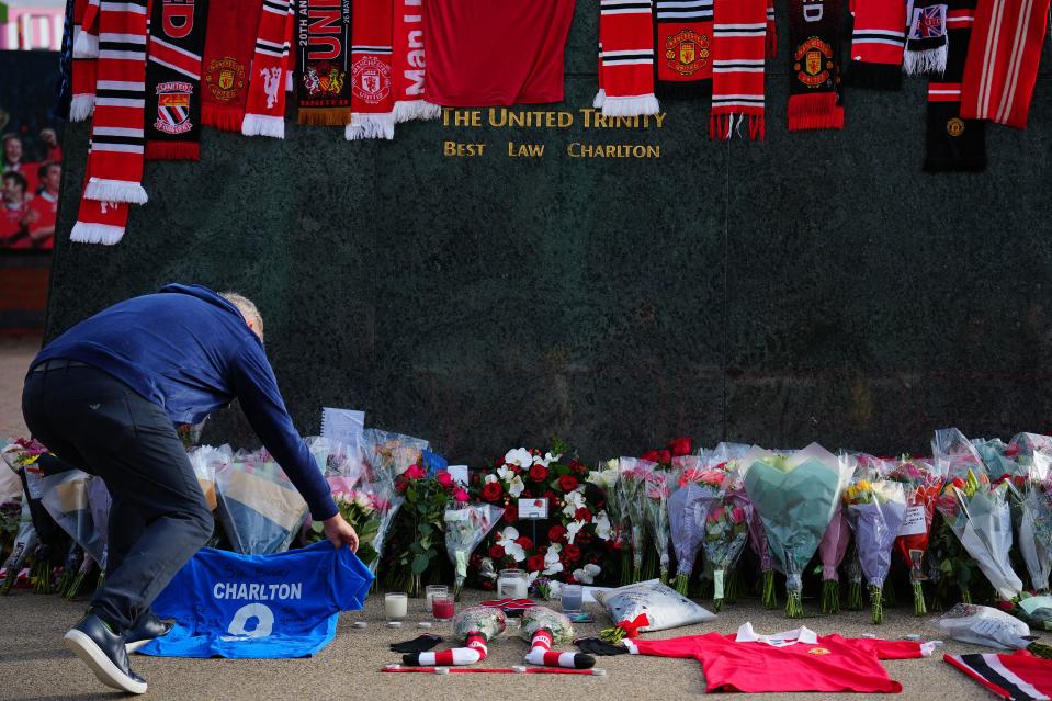 A fan lays a football shirt in tribute at the base of the 'United Trinity' sculpture, depicting former Manchester United players George Best, Denis Law and Bobby Charlton, following the death of Bobby Charlton, outside of Old Trafford football stadium in Manchester, central England, on October 22, 2023. England World Cup winner and Manchester United great Bobby Charlton, described by the club as a 