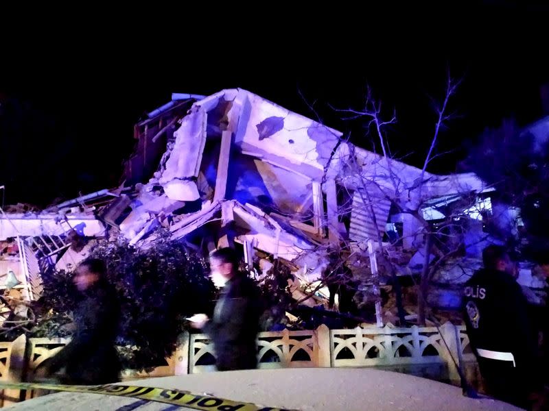 People stand outside a collapsed building after an earthquake in Elazig province