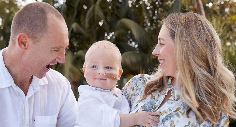 Toddler Noah, who received a rare diagnosis of Pineoblastoma, can be seen with his mum and dad both looking at him and smiling in a photoshoot.