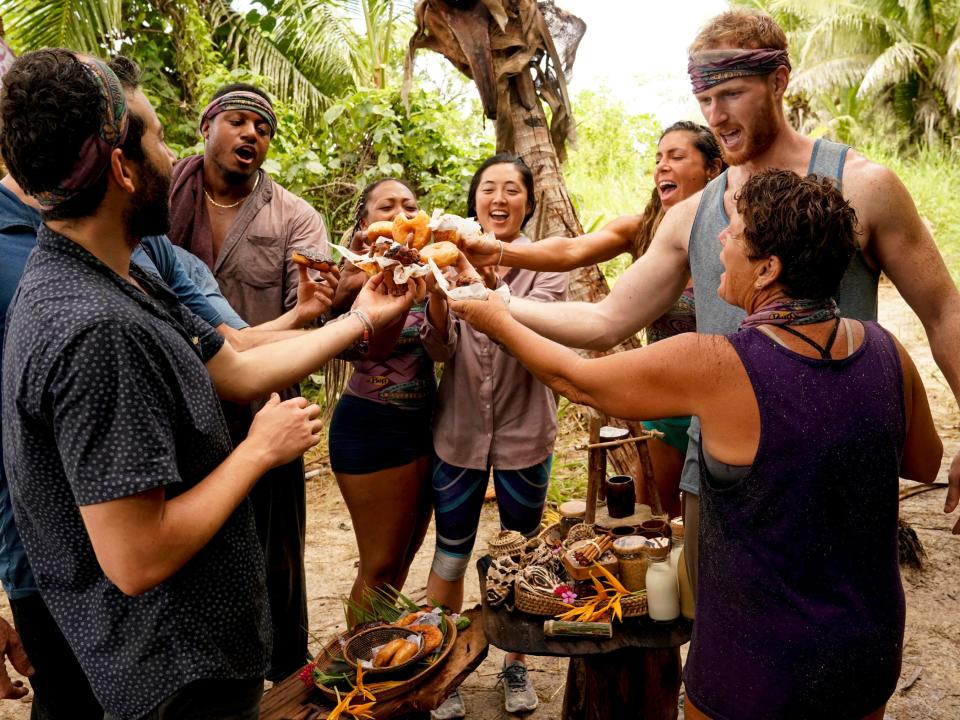 Survivor cast members standing in a circle enjoying food with the jungle in the background