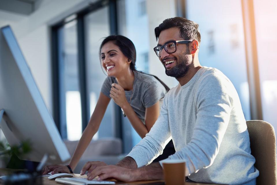 Two investors in an office smile while looking at a computer screen.