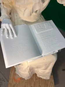 Picture of a statue working model holding a book with Braille translation