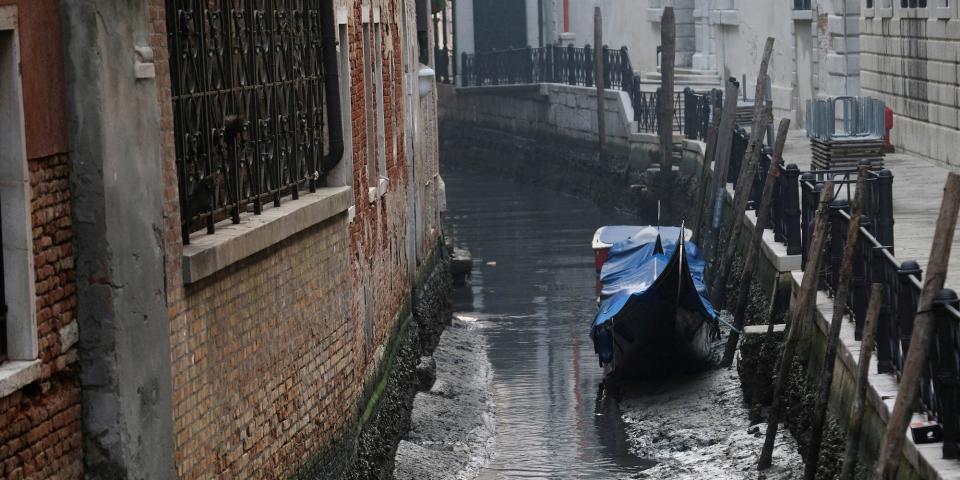 A gondola is pictured in a canal during a severe low tide in the lagoon city of Venice, February 17, 2023.. Just a trickle of water at the bottom.
