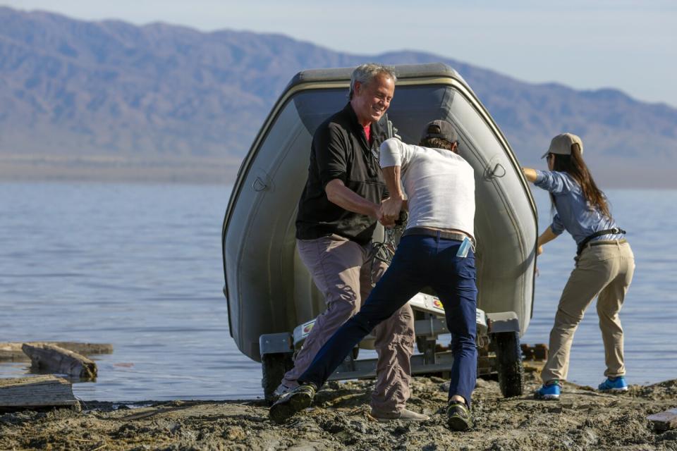 Three people launch a boat into a lake.