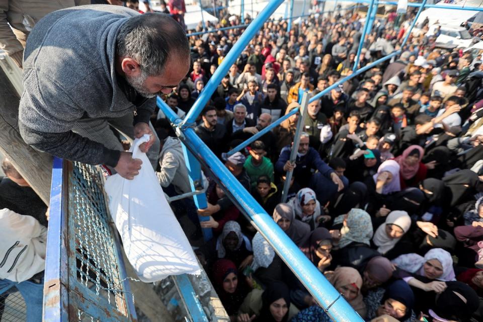 A Palestinian man holds a flour bag as others wait to receive theirs from the United Nations Relief and Works Agency (UNRWA) during a temporary truce between Hamas and Israel, in Khan Younis in the southern Gaza Strip, November 29, 2023. REUTERS/Ibraheem Abu Mustafa  