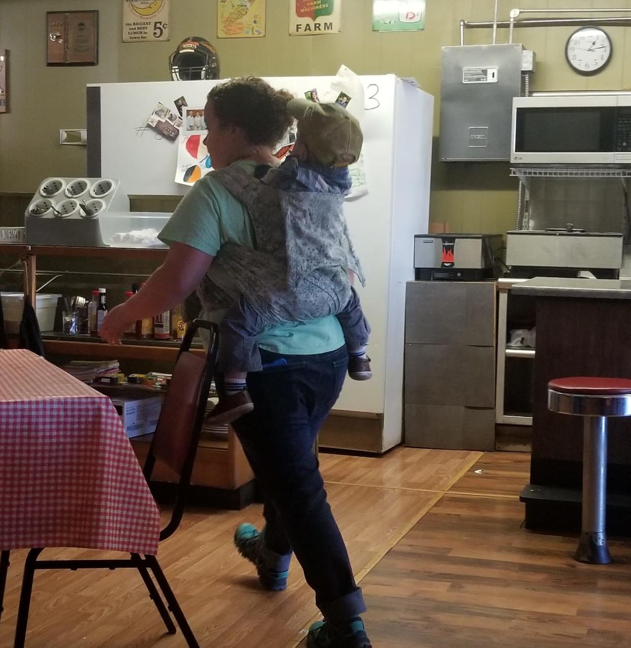 A photo of Kori Dotson, a waitress who worked a busy shift with a toddler strapped to her back, is an inspiration to working mums. (Photo: Kelly Gentry via Facebook)