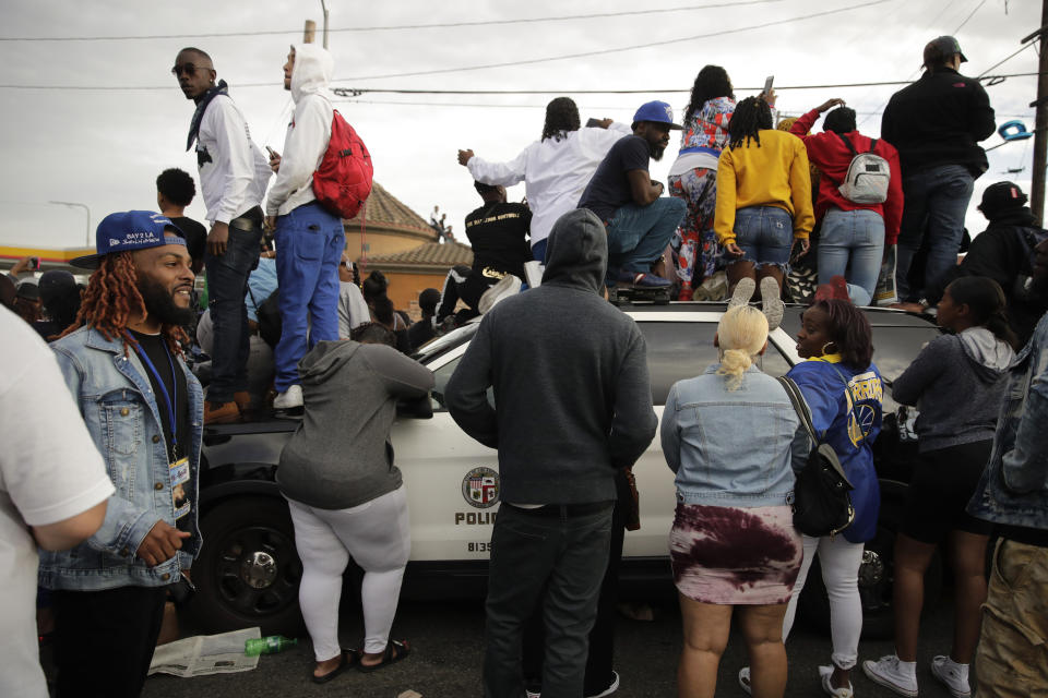People climb on a police vehicle to watch a hearse carrying the casket of slain rapper Nipsey Hussle Thursday, April 11, 2019, in Los Angeles. The 25-mile procession traveled through the streets of South Los Angeles after a memorial service, including a trip past Hussle's clothing store, The Marathon, where he was gunned down March 31. (AP Photo/Jae C. Hong)