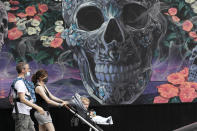 Parents wearing masks walk with their children past a mural, Friday, May 29, 2020, in New York. Gov. Andrew Cuomo says New York City is on track to begin reopening June 8 as the state gradually loosens restrictions put in place during the coronavirus crisis. (AP Photo/Mark Lennihan)