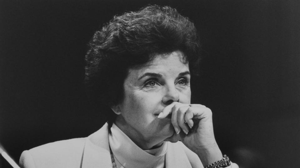 a black and white photo of dianne feinstein sitting and listening to something, with her hand on her mouth