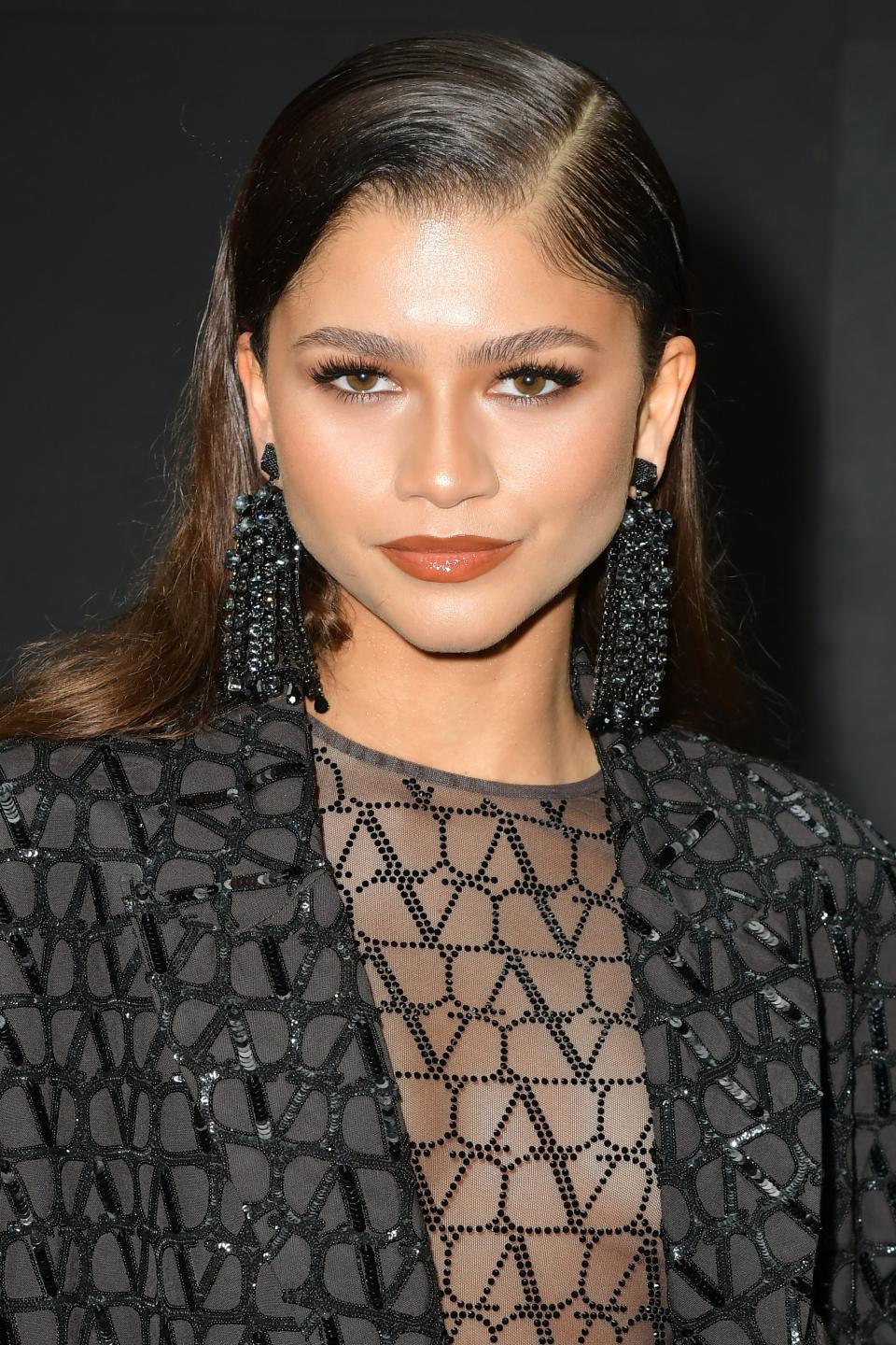 Zendaya in a sheer black outfit with detailed patterns, paired with matching long earrings