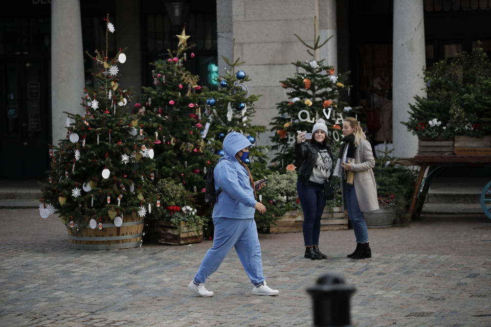 A woman wearing a face mask walks backdropped by Christmas trees in Covent Garden, during England's second coronavirus lockdown in London, Thursday, Nov. 26, 2020. As Christmas approaches, most people in England will continue to face tight restrictions on socializing and business after a nationwide lockdown ends next week, the government announced Thursday. (AP Photo/Matt Dunham)