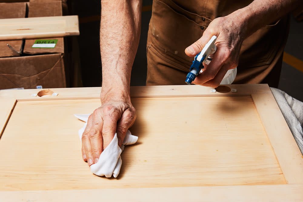 a person using a cloth and spray bottle to clean and prep a part of a kitchen cabinet