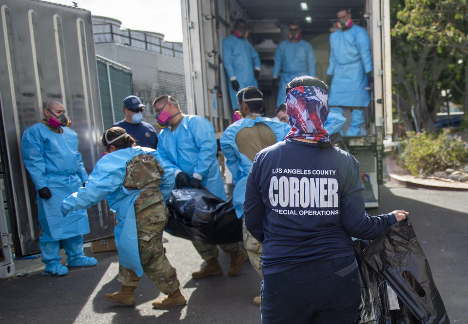 This photo provided by the LA County Dept. of Medical Examiner-Coroner shows Elizabeth "Liz" Napoles, right, works alongside with National Guardsmen who are helping to process the COVID-19 deaths to be placed into temporary storage at LA County Medical Examiner-Coroner Office on Tuesday, Jan. 12, 2020 in Los Angeles. More than 500 people are dying each day in California because of the coronavirus. The death toll has prompted state officials to send more refrigerated trailers to local governments to act as makeshift morgues. State officials said Friday they have helped distribute 98 refrigerated trailers to help county coroners store dead bodies. (LA County Dept. of Medical Examiner-Coroner via AP)