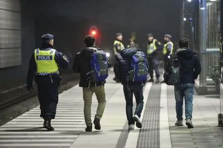 A police officer escorts migrants from a train at Hyllie station outside Malmo, Sweden, in this November 19, 2015 file photo. Thousands of Iraqi refugees who arrived in Finland last year have decided to cancel their asylum applications and to return home voluntarily, citing family issues and disappointment with life in the frosty Nordic country. REUTERS/Johan Nilsson/TT NEWS AGENCY/Files