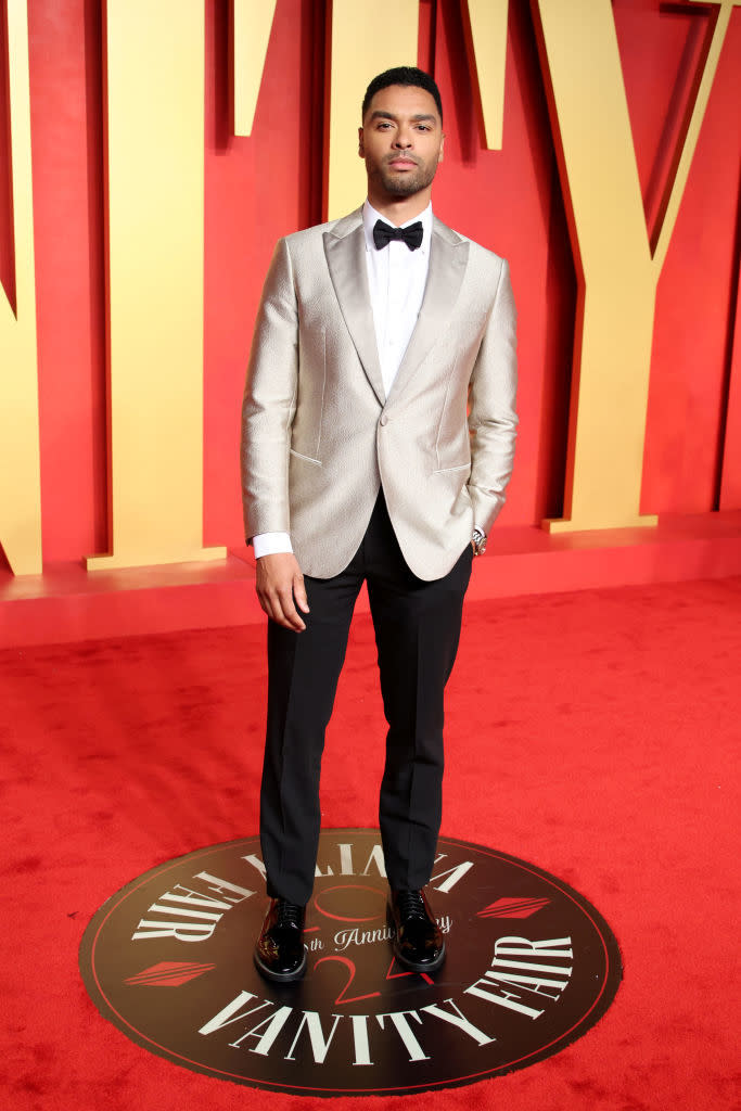 Man in a silver blazer and black trousers with bow tie stands on Vanity Fair carpet