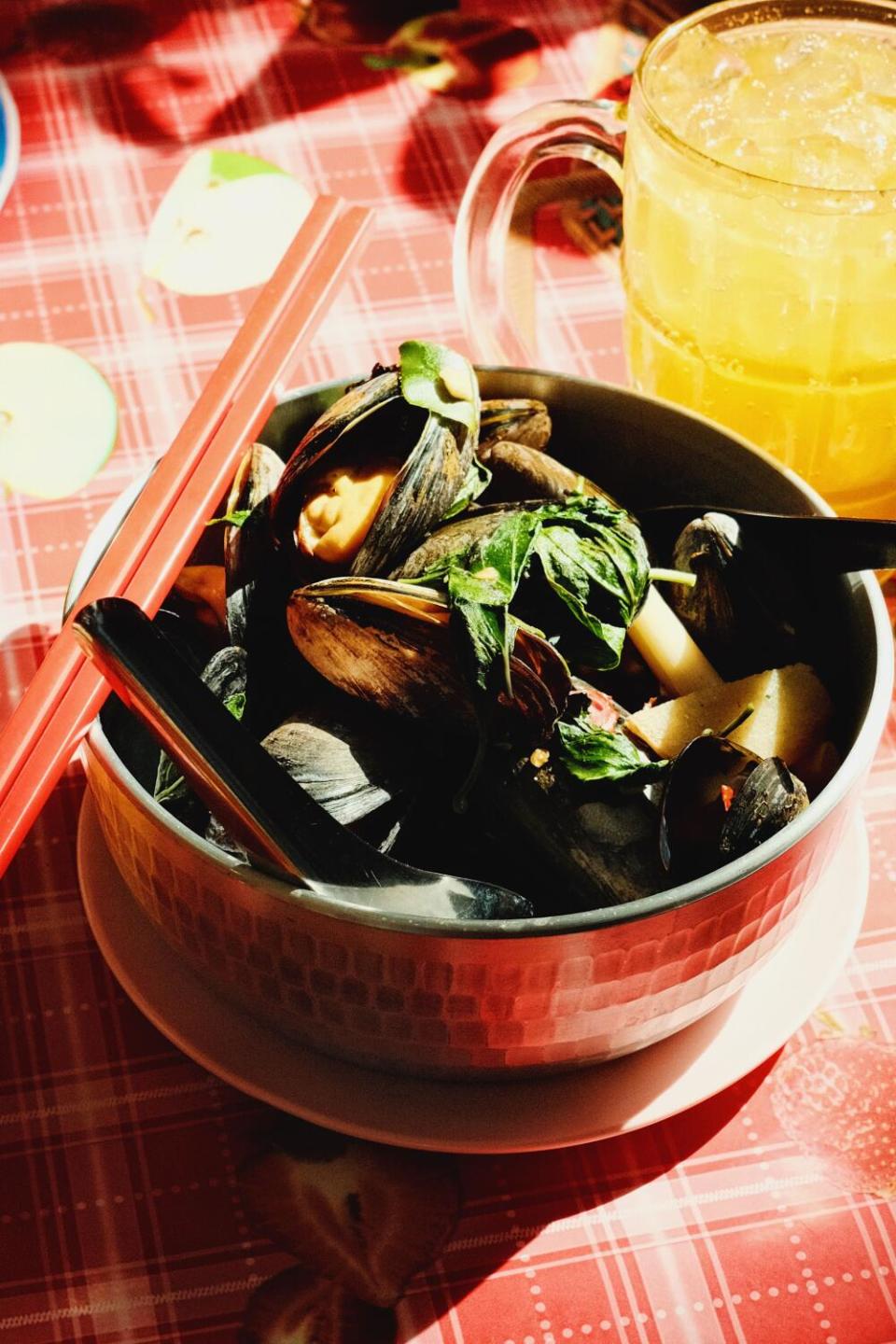 A vertical photo of a bowl of lemongrass mussels with red chopsticks on a red patterned tablecloth at Holy Basil Atwater