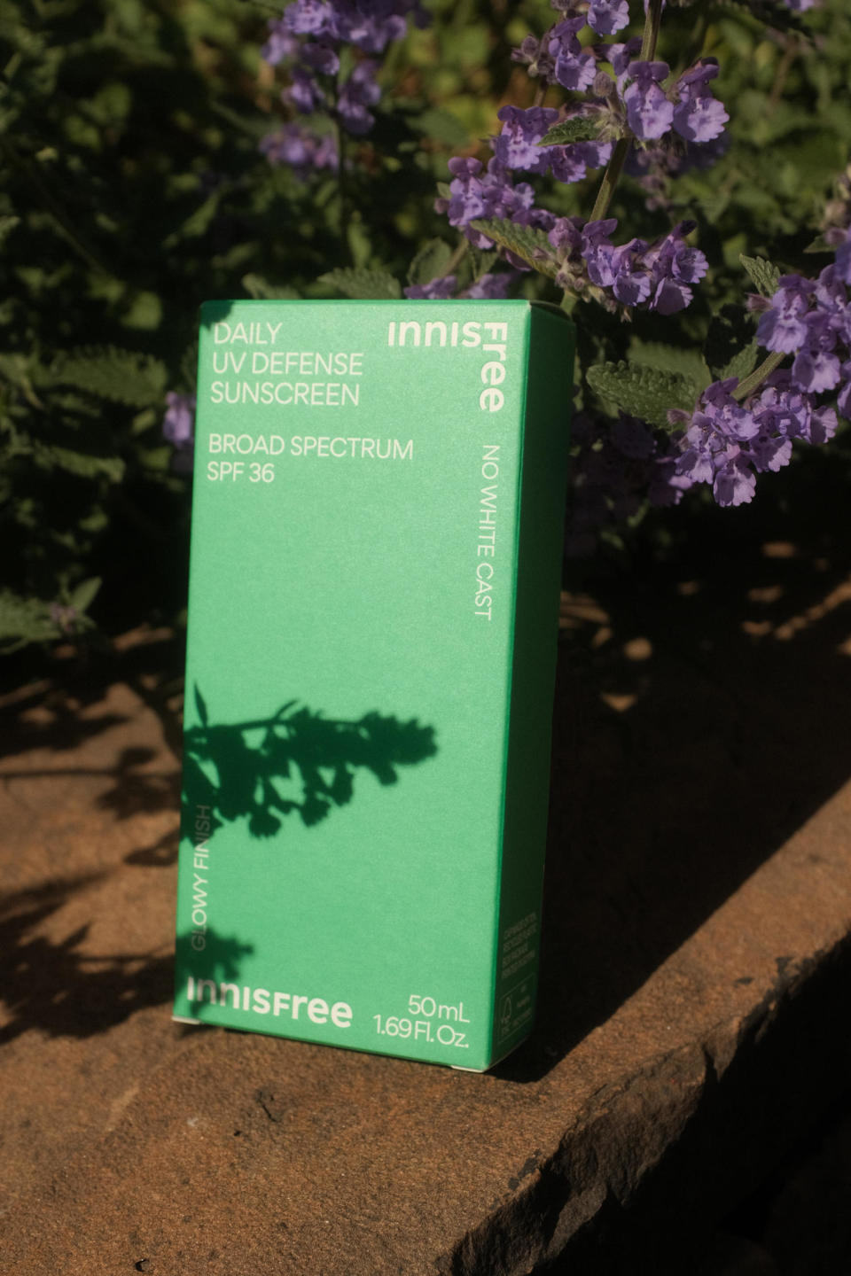 A box containing a bottle of sunscreen amidst purple flowers and leaves. (Chelsea Stahl and Elise Wrabetz / NBC News)