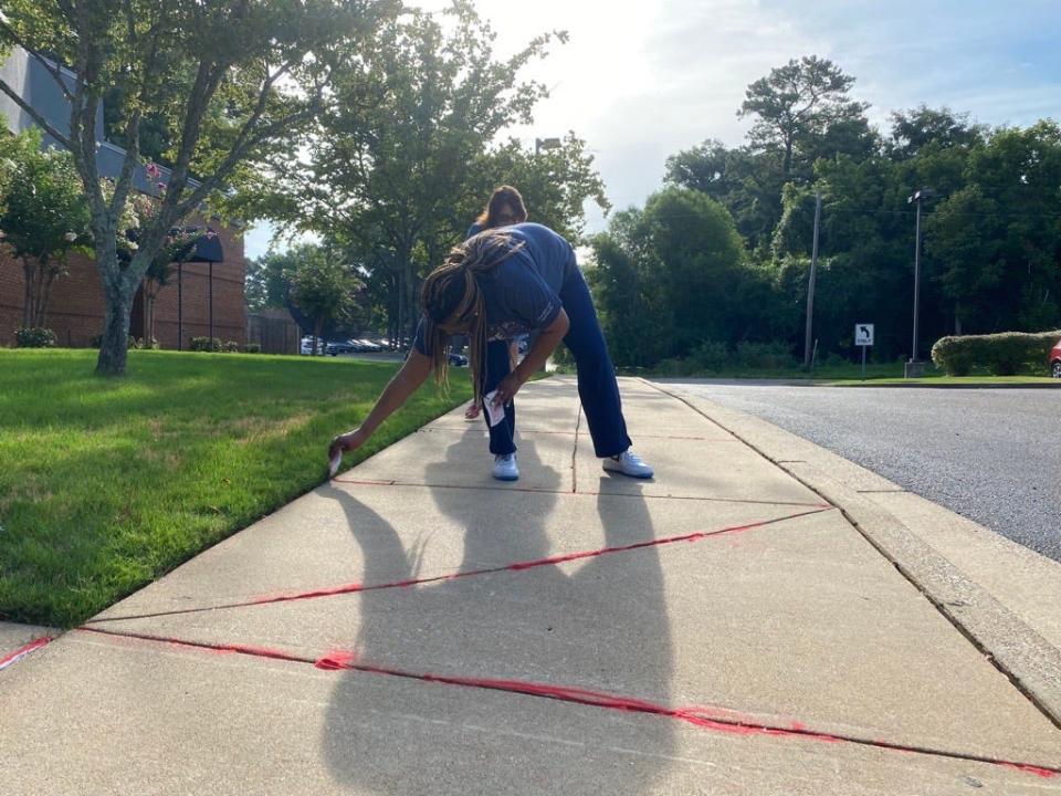 Members of the Jackson-Madison County Regional Health Department poured red sand into the cracks of the department's sidewalks to draw attention to the victims that “fall through the cracks” of society.