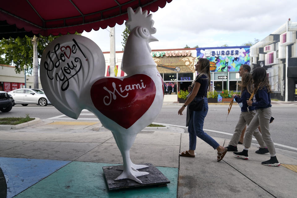 People walk past a sculpture of a rooster along Calle Ocho, Tuesday, Nov. 16, 2021, in the Little Havana neighborhood in Miami. Cooped-up tourists eager for a taste of Florida's sandy beaches, swaying palm trees and warmer climates are visiting the Sunshine State in droves, topping pre-pandemic levels in recent months. (AP Photo/Lynne Sladky)