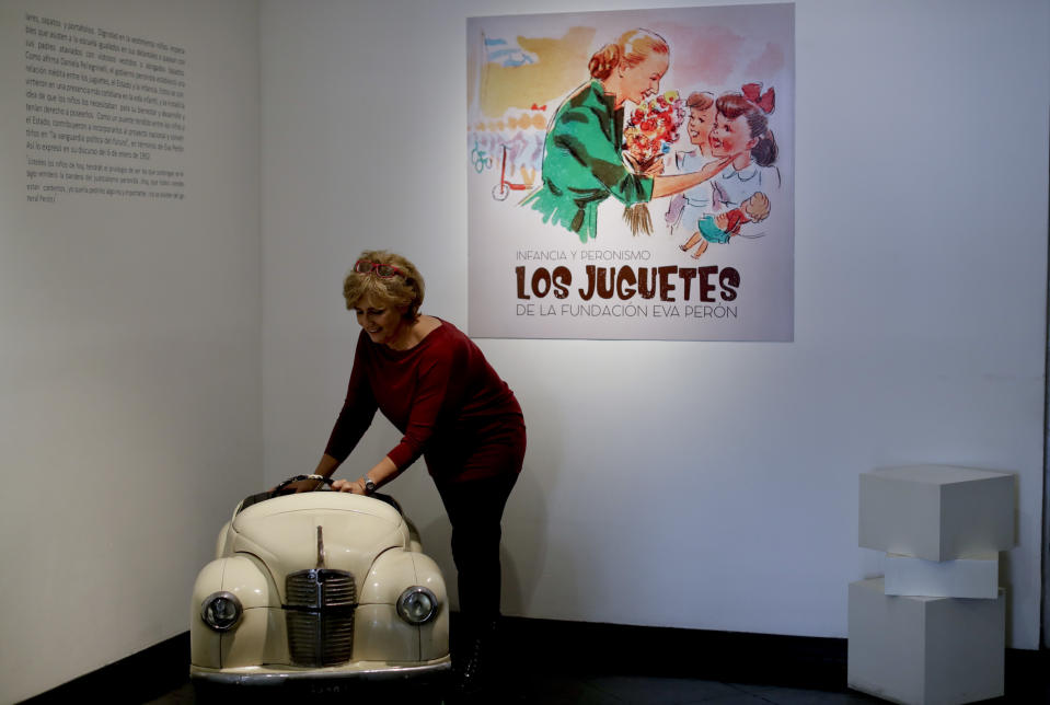 Marcela Genés, curator of the Evita museum, poses for a photo with a toy pedal car at the "Childhood and Peronism, the toys of the Eva Perón Foundation" exhibit, in Buenos Aires, Argentina, Wednesday, April 17, 2019. "Children were always given particular importance in Eva's work, especially all matters concerning children's rights," Genés said. (AP Photo/Natacha Pisarenko)