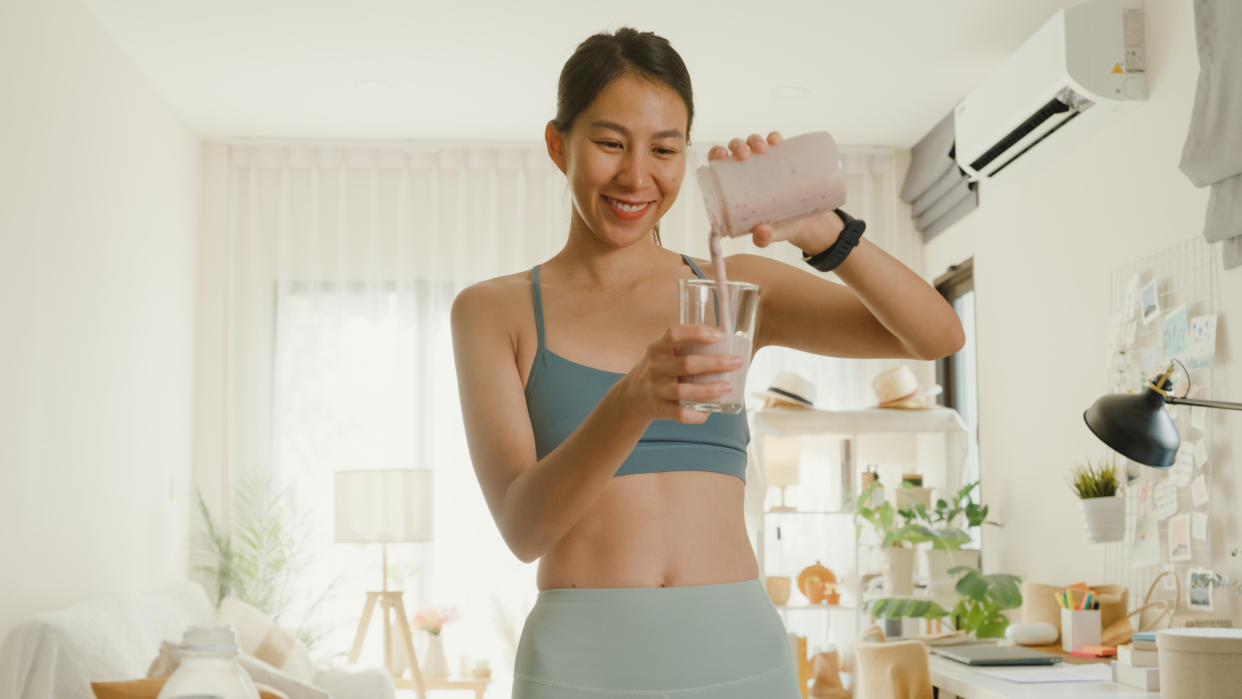 Young Asian athletic woman using blender and pouring smoothie to glass at home. Healthy food concept, health supplements.