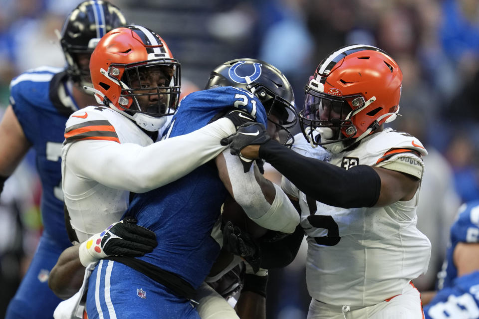 Indianapolis Colts running back Zack Moss (21) is tackled by Cleveland Browns defensive end Ogbo Okoronkwo, left, and linebacker Anthony Walker Jr. (5) during the first half of an NFL football game, Sunday, Oct. 22, 2023, in Indianapolis. (AP Photo/Michael Conroy)