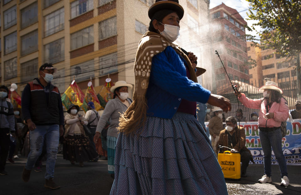 A woman sprays disinfectant on demonstrators amid the COVID-19 pandemic, during a march asking for free internet access and computers from the government, so that their children can take online classes, in La Paz, Bolivia, Monday, May 10, 2021. (AP Photo/Juan Karita)