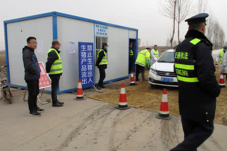 Police officers and workers in protective suits are seen at a checkpoint on a road leading to a farm owned by Hebei Dawu Group where African swine fever was detected, in Xushui district of Baoding, Hebei province, China February 26, 2019. REUTERS/Hallie Gu