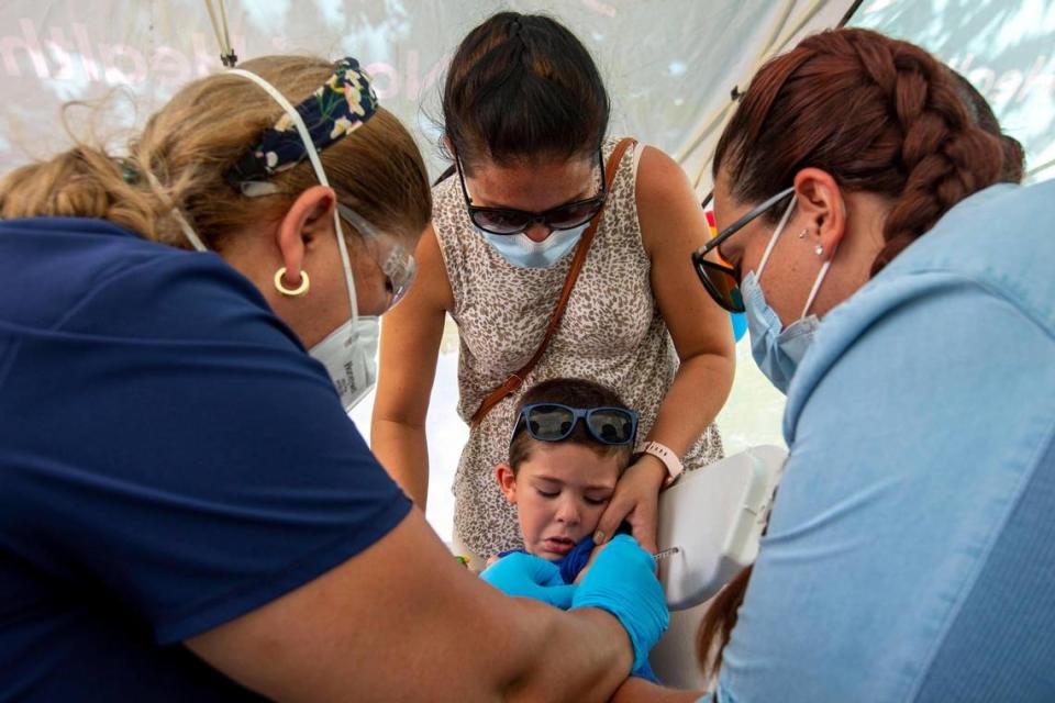 Giam Diaz, 3, receives a COVID-19 vaccine as his mother, Ismarai Rodriguez, 37, center, and his aunt Natalie Leon, 30, right, hold him Saturday at the Nomi Health Mobile Health Unit at Tropical Park. The county has begun offering the free vaccines to children under 5 at eight sites.