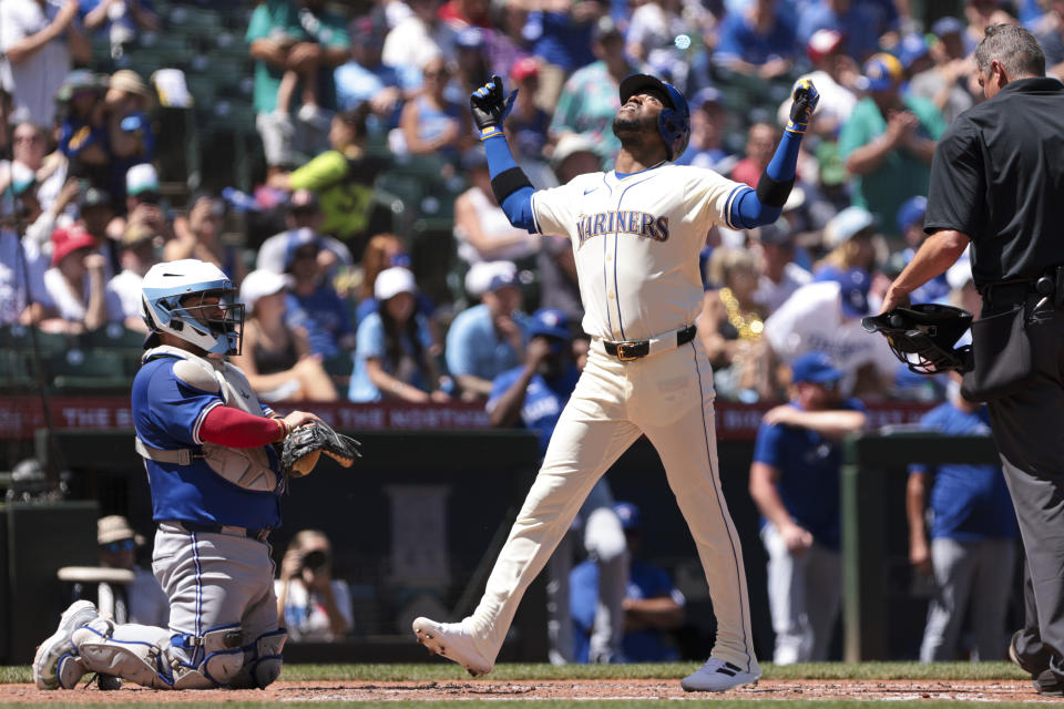 Seattle Mariners' Victor Robles, center, celebrates at home plate after hitting a solo home run as Toronto Blue Jays catcher Alejandro Kirk, left, looks on during the third inning of a baseball game, Sunday, July 7, 2024, in Seattle. (AP Photo/Jason Redmond)