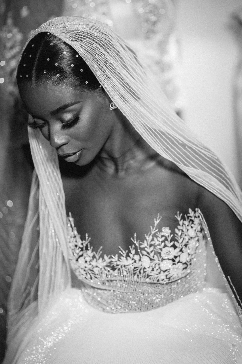 A black and white photo of a bride looking down with a veil and gems in her hair.