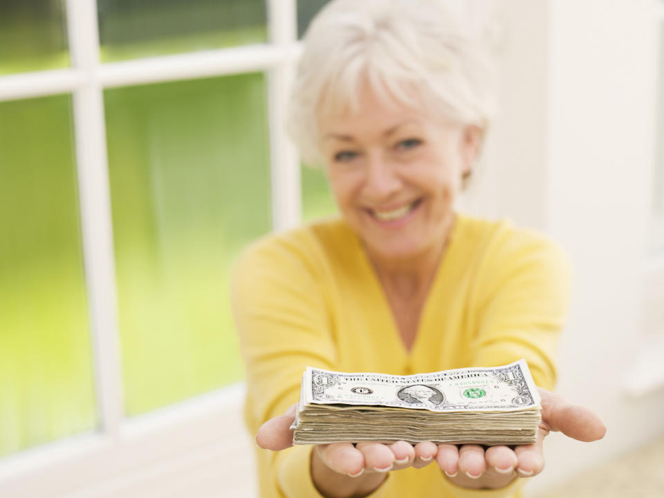 A smiling senior woman holding out a neat stack of cash in her hands.